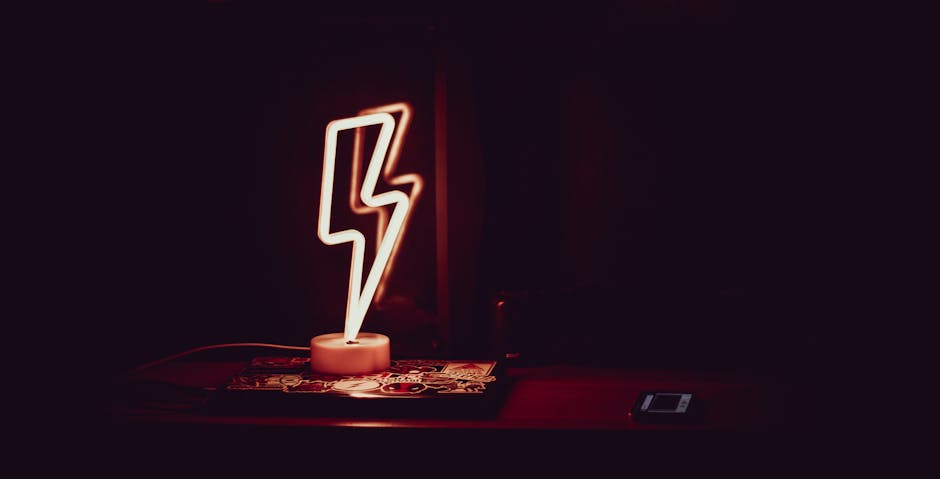 Modern neon night light in shape of lightning placed on table and reflected in mirror in dark room